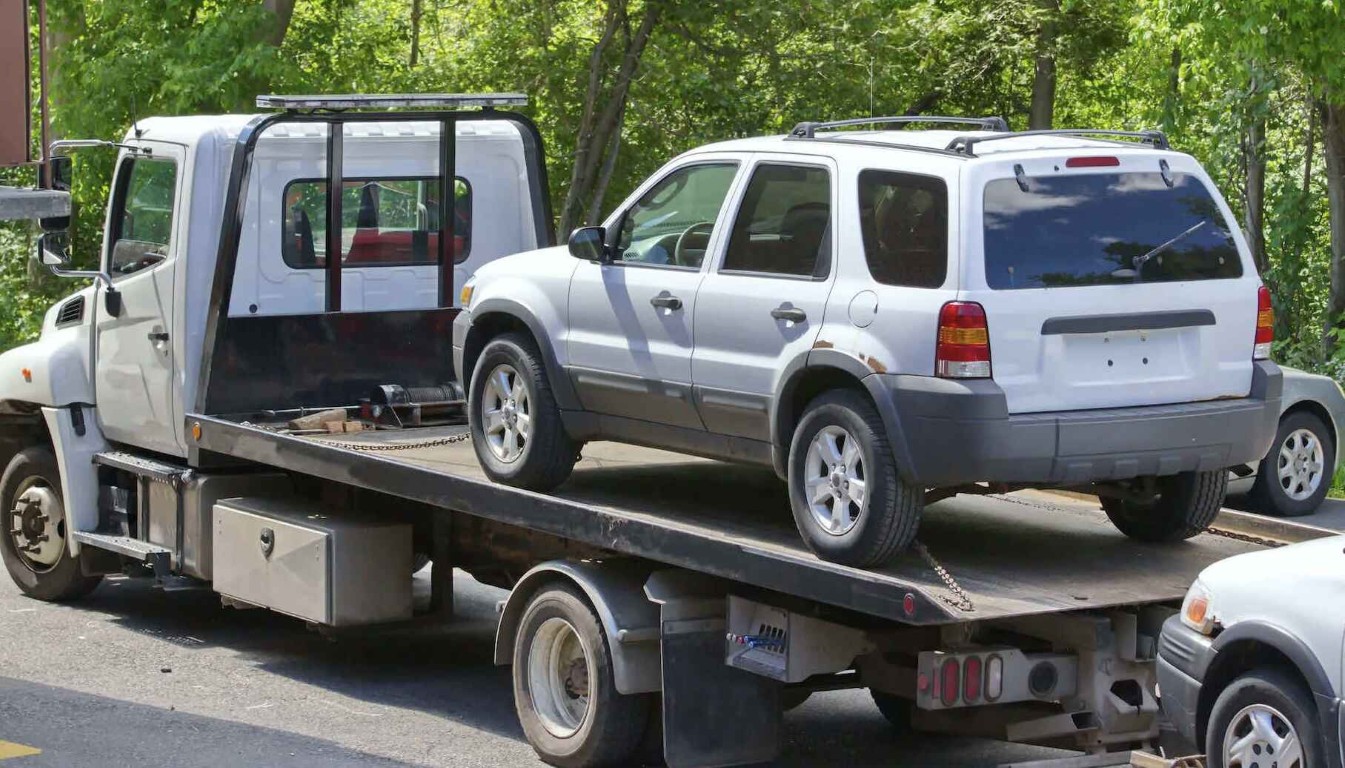 Professional roadside assistance loading white SUV on specialized flatbed tow truck in Hollister, CA